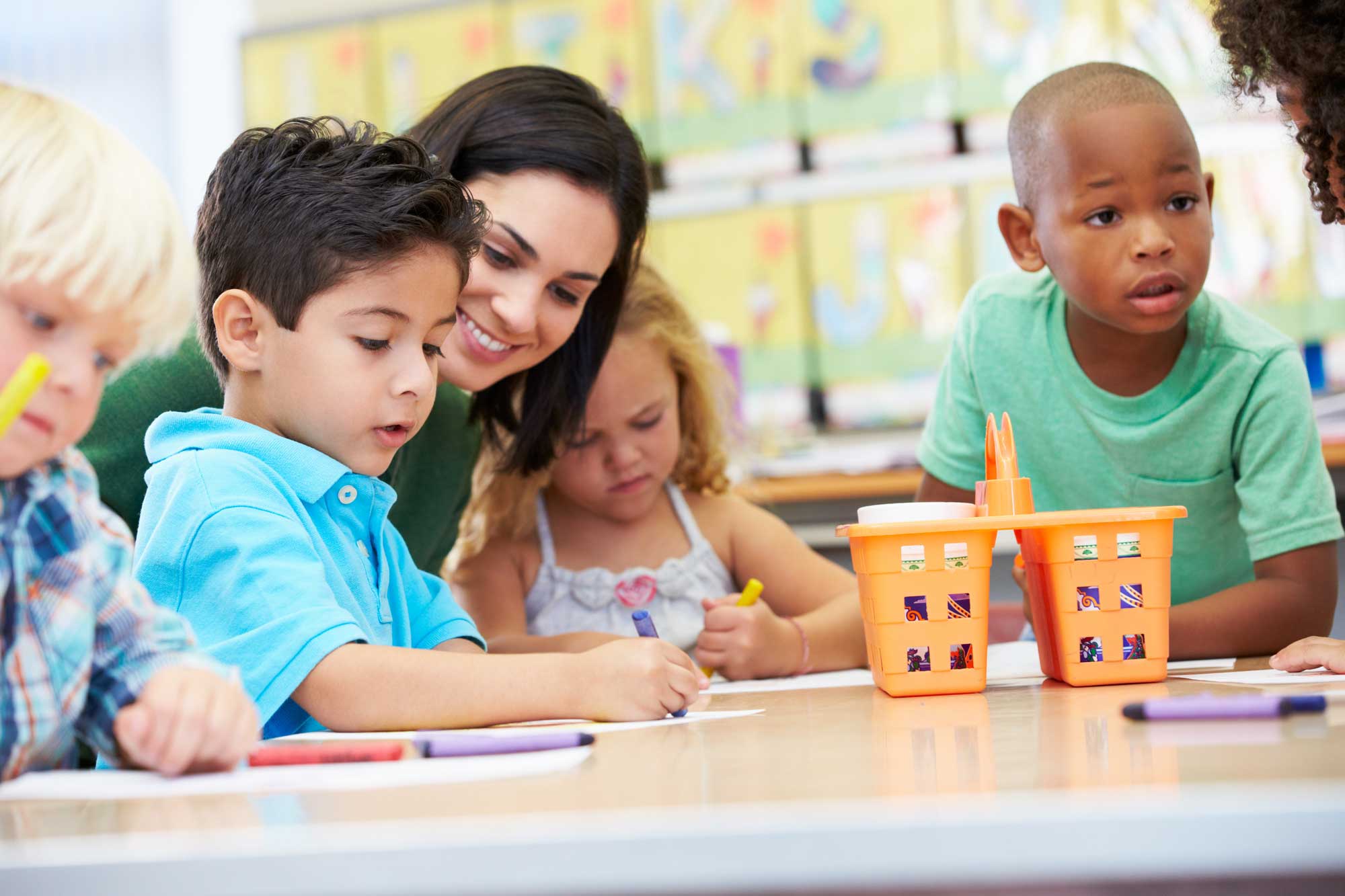 kids coloring with crayons with their teacher